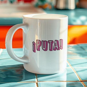 May include: White ceramic mug with a pink exclamation point and the word "PUTA!" printed on it. The mug is sitting on a blue tiled surface.