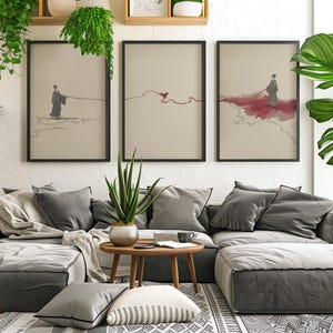 May include: Three framed art prints depict a figure connected to a red line, set against a neutral background. The artwork hangs above a gray sectional sofa with decorative pillows. The room is decorated with plants and a patterned rug.