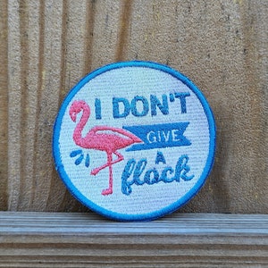 May include: A blue and white embroidered patch with a pink flamingo and the text "I don't give a flock".