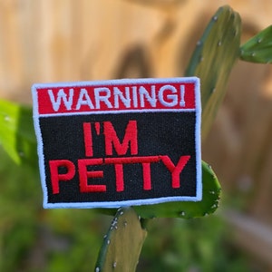 May include: A white and red warning patch with black text that reads "WARNING! I'M PETTY".