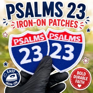 May include: Two shield-shaped iron-on patches featuring a red top section with the white text PSALMS and a blue bottom section with the white number 23. The design mimics a highway sign. The patches have a white border and are held in a hand.