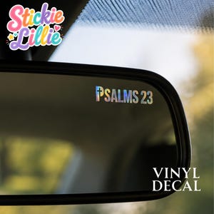 May include: A holographic vinyl decal applied to a car rearview mirror, featuring the text "PSALMS 23" with a cross symbol replacing the letter P. The decal has a reflective, multi-colored finish that shifts in appearance under light.