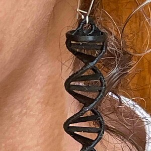 May include: Black dangle earrings featuring a 3D DNA helix design. The earrings are made of a black material and have a silver hook.