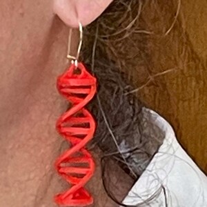 May include: Red 3D printed DNA helix earrings. The earrings are dangling and have a gold hook.