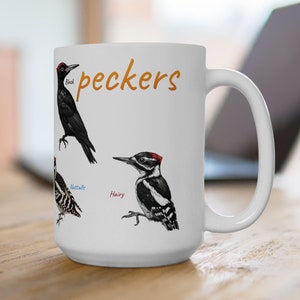 May include: White ceramic mug with a black, red, and white woodpecker illustration. The mug has the word "peckers" printed in orange on the front. The woodpecker is labeled "Hairy".