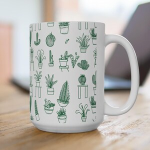 Peut inclure: Une tasse en céramique blanche avec un motif de plantes en pot vert et blanc. La tasse a une anse sur le côté droit.