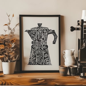 以下が含まれることがあります： 複雑なデザインが施されたコーヒーポットの白黒プリント。額縁に入れて壁にかけられており、その下には木製カウンターがあり、コーヒーメーカーとマグカップが置かれている。