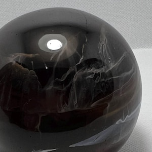 May include: A black glass sphere with a white and grey swirling pattern inside. The sphere has a smooth, glossy finish.