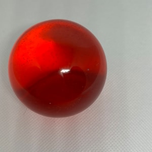 May include: A bright red glass sphere with a smooth, shiny surface.