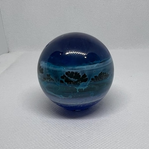 May include: A blue glass sphere with white and black swirling patterns inside. The sphere is smooth and reflective.