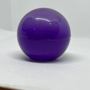 May include: A large, round, purple glass ball. The ball is smooth and shiny.