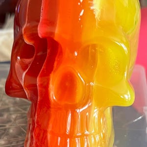 May include: A clear glass skull with a red, orange, and yellow gradient. The skull is made of glass and has a smooth, shiny finish.