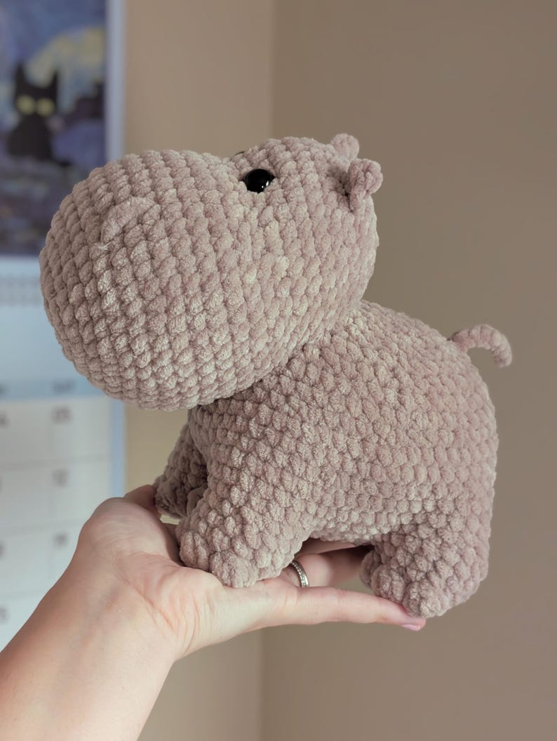 May include: A soft, brown crocheted hippopotamus plush toy. The hippo is standing on its four legs and has a small, black eye.