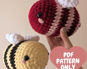 May include: Two crocheted bee plushies. One is red and pink with white wings, the other is yellow and black with white wings. The text "PDF PATTERN ONLY" is on a pink heart.