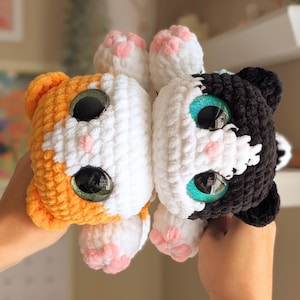 May include: Two crocheted cat plushies, one orange and white, the other black and white. Both have large, glittery eyes and pink paw pads. The plushies are handmade and have a soft, textured appearance.