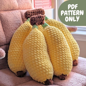 May include: Crocheted corn-shaped pillows in shades of yellow, brown, and green. The pillows are arranged on a pink surface. The image includes the text "PDF PATTERN ONLY" in a green circle.