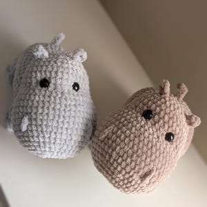 May include: Two crocheted hippopotamus plushies, one gray and one brown, with black eyes.