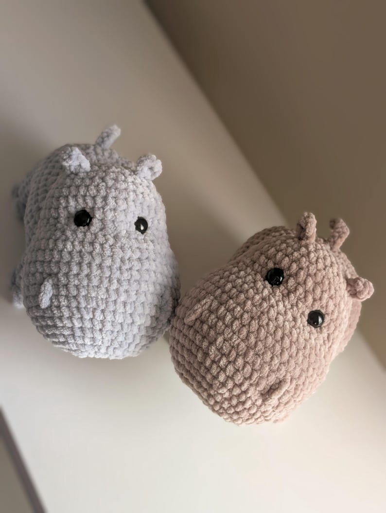 May include: Two crocheted hippopotamus plushies, one gray and one brown, with black eyes.