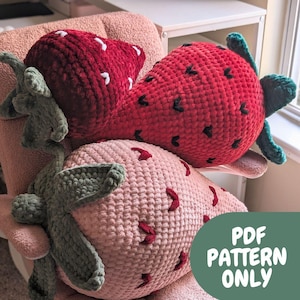 May include: Two crocheted strawberry cushions, one red and one pink, with green leaves. The cushions are on a chair and the text "PDF PATTERN ONLY" is in the bottom right corner of the image.