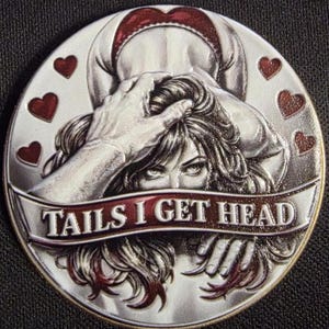 May include: A silver-colored coin with a detailed illustration. The coin features a woman's face and hands, with the text "TAILS I GET HEAD" on a banner. Red heart shapes are placed around the edge of the coin.
