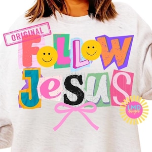 Könnte beinhalten: Ein hellgraues Sweatshirt mit dem Schriftzug "FOLLOW JESUS" in bunten Blockbuchstaben. Das Design umfasst Smiley-Gesichter, eine rosa Schleife und das Wort "ORIGINAL" in einem rosa Stempel.