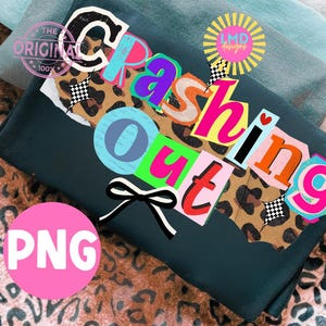 以下が含まれることがあります： 「Crashing Out」の文字がカラフルな切り抜き文字でデザインされた、濃い緑色の折り畳まれたシャツ。 レオパード柄のアクセント、白黒のリボン、ピンクの「PNG」サークルが含まれています。
