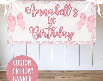 May include: A pink and white custom birthday banner with the text "Annabell's 1st Birthday" and two pink bows on either side.