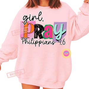 May include: A light pink sweatshirt with the words "girl. PRAY Philippians 4:6" in a colorful design. The word "PRAY" is in a black, orange, pink, and green block design. The sweatshirt has long sleeves.