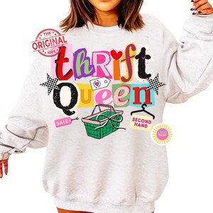 May include: A light gray sweatshirt with the words "thrift queen" in colorful, playful lettering. The design includes a shopping basket, stars, and the words "sale" and "second hand". A stamp reads "The Original 100%."