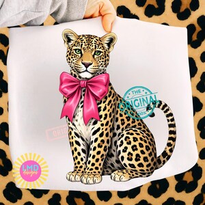 May include: A digitally illustrated leopard with a large pink bow around its neck. The leopard has a spotted coat, green eyes, and is sitting upright. The image includes the text "THE ORIGINAL" and "LMD designs".