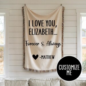 May include: A white throw blanket with black text that reads "I love you, Elizabeth... Forever & Always -Matthew". A black heart is above the name Matthew. The blanket has a fringe border.