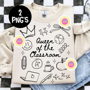 May include: A beige sweatshirt with black line art illustrations and the text "Queen of the Classroom." The design includes a crown, push pins, a bow, a globe, a smiley face, a paperclip, an A+, a coffee cup, an apple, a laptop, a pen, and math symbols.