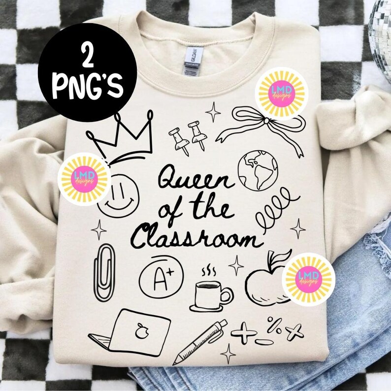 May include: A beige sweatshirt with black line art illustrations and the text "Queen of the Classroom." The design includes a crown, push pins, a bow, a globe, a smiley face, a paperclip, an A+, a coffee cup, an apple, a laptop, a pen, and math symbols.
