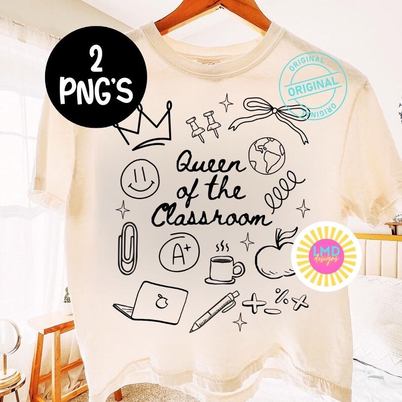 May include: Cream-colored t-shirt with a black graphic design featuring a crown, a smiley face, and the words "Queen of the Classroom." Other illustrations include a globe, apple, and a coffee cup.