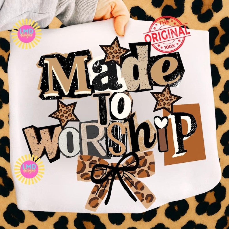 K&ouml;nnte beinhalten: Wei&szlig;es Grafik-T-Shirt mit den Worten "Made to Worship" in einer Mischung aus Schriftarten und Farben, darunter schwarze, braune und Leopardenmuster-Akzente. Mit einer Schleife und Sternformen. Der Text "The Original" ist oben rechts aufgestempelt.