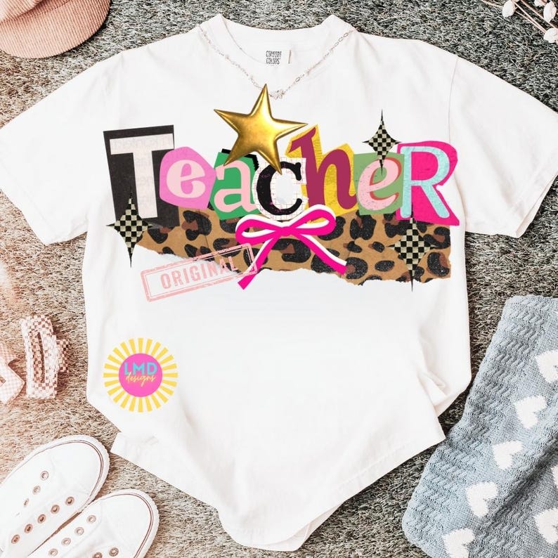 May include: White t-shirt with the word "Teacher" in colorful, layered letters, a gold star, and a leopard print design. The shirt also features a pink bow and the text "ORIGINAL". A sunburst logo with "LMD designs" is visible.