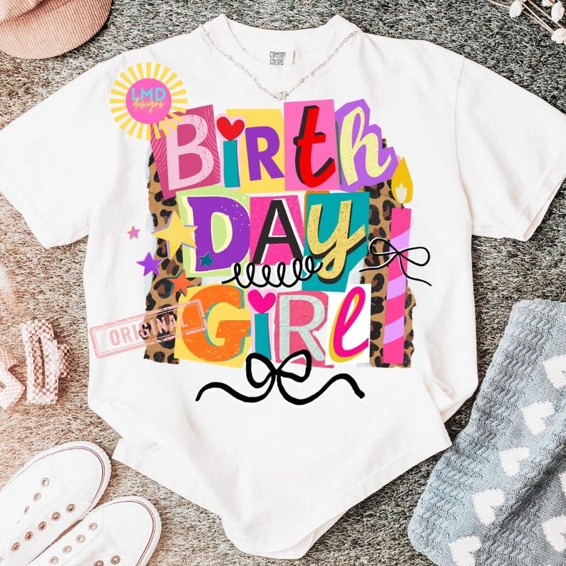 May include: White t-shirt with a colorful "Birthday Girl" graphic. The design features the words "Birthday Girl" in various colors and fonts, with stars, hearts, and a bow. The shirt has a crew neck and short sleeves.