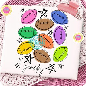May include: A white surface featuring a colorful graphic print of multiple American footballs in pink, brown, green, blue, purple, orange, yellow, and lime green, interspersed with black hand-drawn stars and the word gameday in black script.