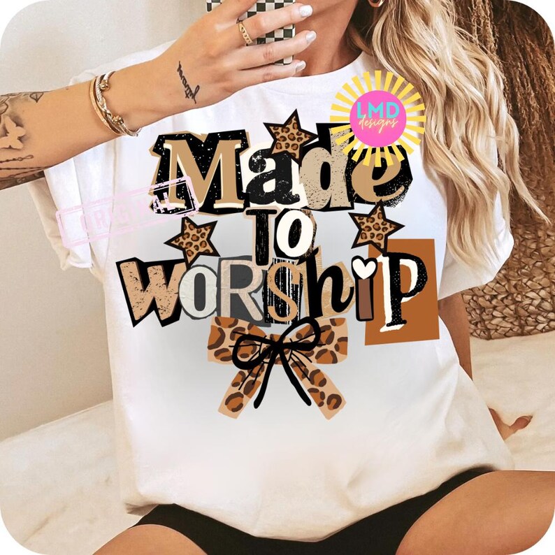 K&ouml;nnte beinhalten: Wei&szlig;es T-Shirt mit dem Text "Made to Worship" in einer Mischung aus Schriftarten und Farben, darunter braune, schwarze und Leopardenmuster-Akzente. Das Design zeigt Sterne und eine Schleife. Das T-Shirt hat kurze &Auml;rmel.