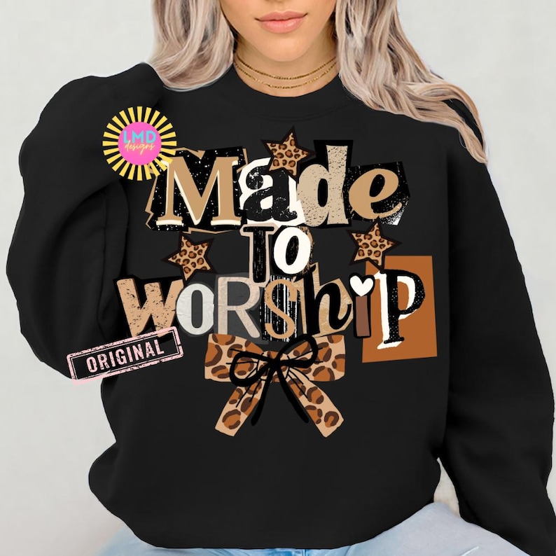 K&ouml;nnte beinhalten: Schwarzes Sweatshirt mit dem Text "Made to Worship" in einer Mischung aus Schriftarten und Farben, einschlie&szlig;lich braunen, wei&szlig;en und Leopardenmuster-Akzenten. Eine Schleife mit Leopardenmuster befindet sich unten. Das Sweatshirt hat einen Rundhalsausschnitt.