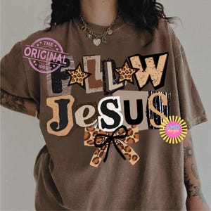 K&ouml;nnte beinhalten: Braunes T-Shirt mit dem Schriftzug "FOLLOW JESUS" im Collage-Stil. Die Buchstaben haben verschiedene Muster, darunter Leopardenmuster und eine Schleife. Ein rosa Stempel mit der Aufschrift "THE ORIGINAL 100%" befindet sich oben links.