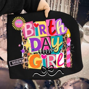 May include: Black tote bag with a colorful "Birthday Girl" design. The design includes the words "Birthday Girl" in various colors, stars, hearts, and a bow. The bag also has a "LMD designs" logo and the word "ORIGINAL".