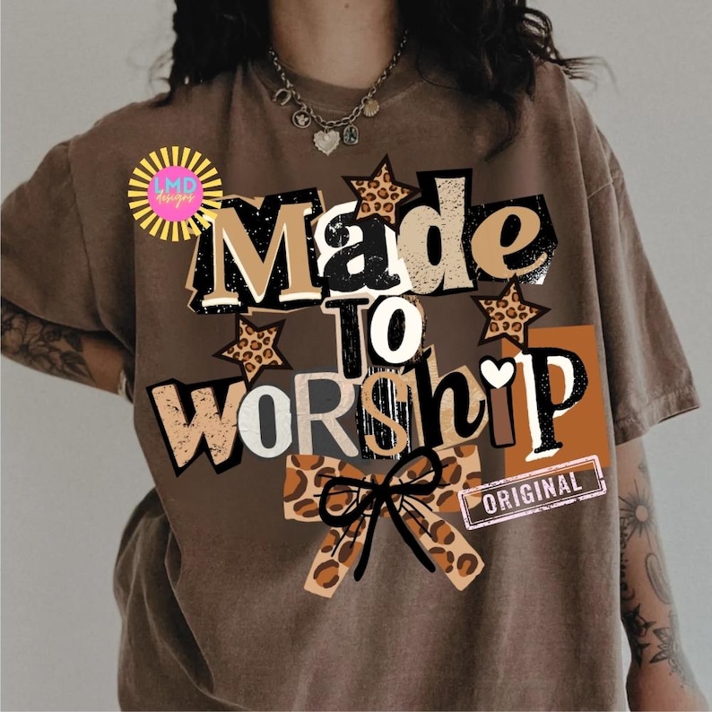 K&ouml;nnte beinhalten: Braunes T-Shirt mit dem Schriftzug "Made to Worship" in einem mehrschichtigen Design mit Leopardensternchen und einer Schleife. Das Wort "Original" ist auf einem kleinen rechteckigen Etikett aufgedruckt.