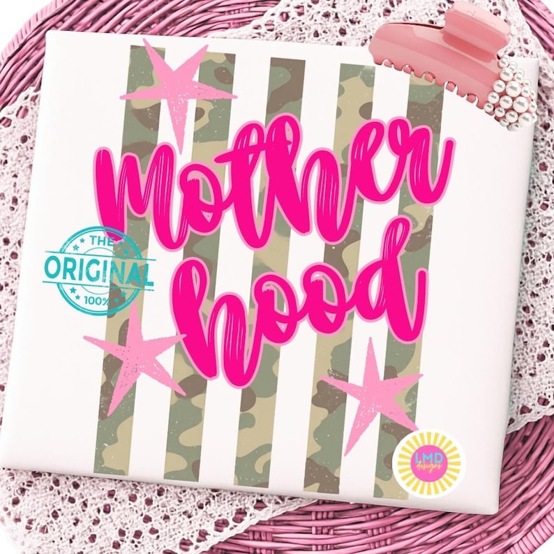 May include: A white canvas with the word "Motherhood" in bright pink script, accented with pink star shapes and a camouflage stripe design. The canvas also features the text "The Original 100%" and a small logo.