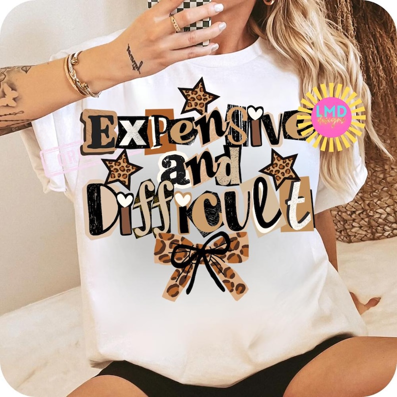 Pu&ograve; includere: T-shirt bianca con la scritta "Expensive and Difficult" in un mix di font e colori, tra cui accenti marroni, neri e stampa leopardata. Il design include stelle e un fiocco.