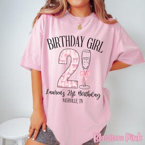 Może przedstawiać: R&oacute;żowa koszulka z napisem "Birthday Girl" i dużą cyfrą "2" ozdobioną r&oacute;żowymi kokardkami. Pod cyfrą znajduje się napis "Lauren's 21st Birthday Nashville, TN".