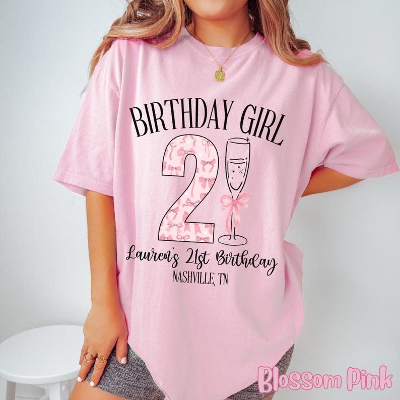 Może przedstawiać: R&oacute;żowa koszulka z napisem "Birthday Girl" i dużą cyfrą "2" ozdobioną r&oacute;żowymi kokardkami. Pod cyfrą znajduje się napis "Lauren's 21st Birthday Nashville, TN".