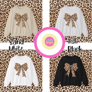May include: Four sweatshirts in sand white, ash, white, and black, each featuring a large bow with a leopard print design. The image includes the text "Sand White", "Ash Black", and the logo "LMD designs".