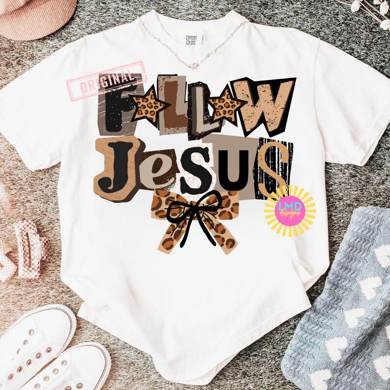 K&ouml;nnte beinhalten: Wei&szlig;es T-Shirt mit dem Schriftzug "Follow Jesus" in einer Mischung aus Schriftarten und Farben, darunter Braun, Schwarz und Leopardenmuster. Eine Schleife mit Leopardenmuster befindet sich unten. Das Shirt hat eine lockere Passform.