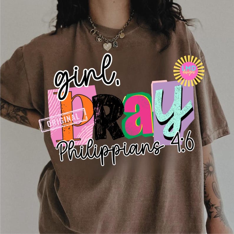May include: Brown t-shirt with the words "girl. PRAY" in a colorful, block letter design. The text "Philippians 4:6" is below the word "PRAY". The shirt has a vintage, worn look.